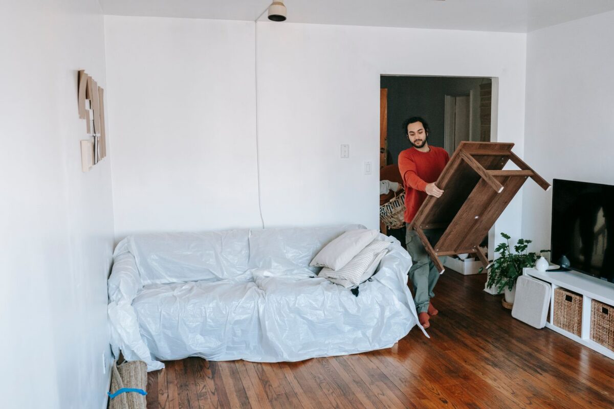 Wooden furniture carried through a living room, with a sofa wrapped in protective sheeting