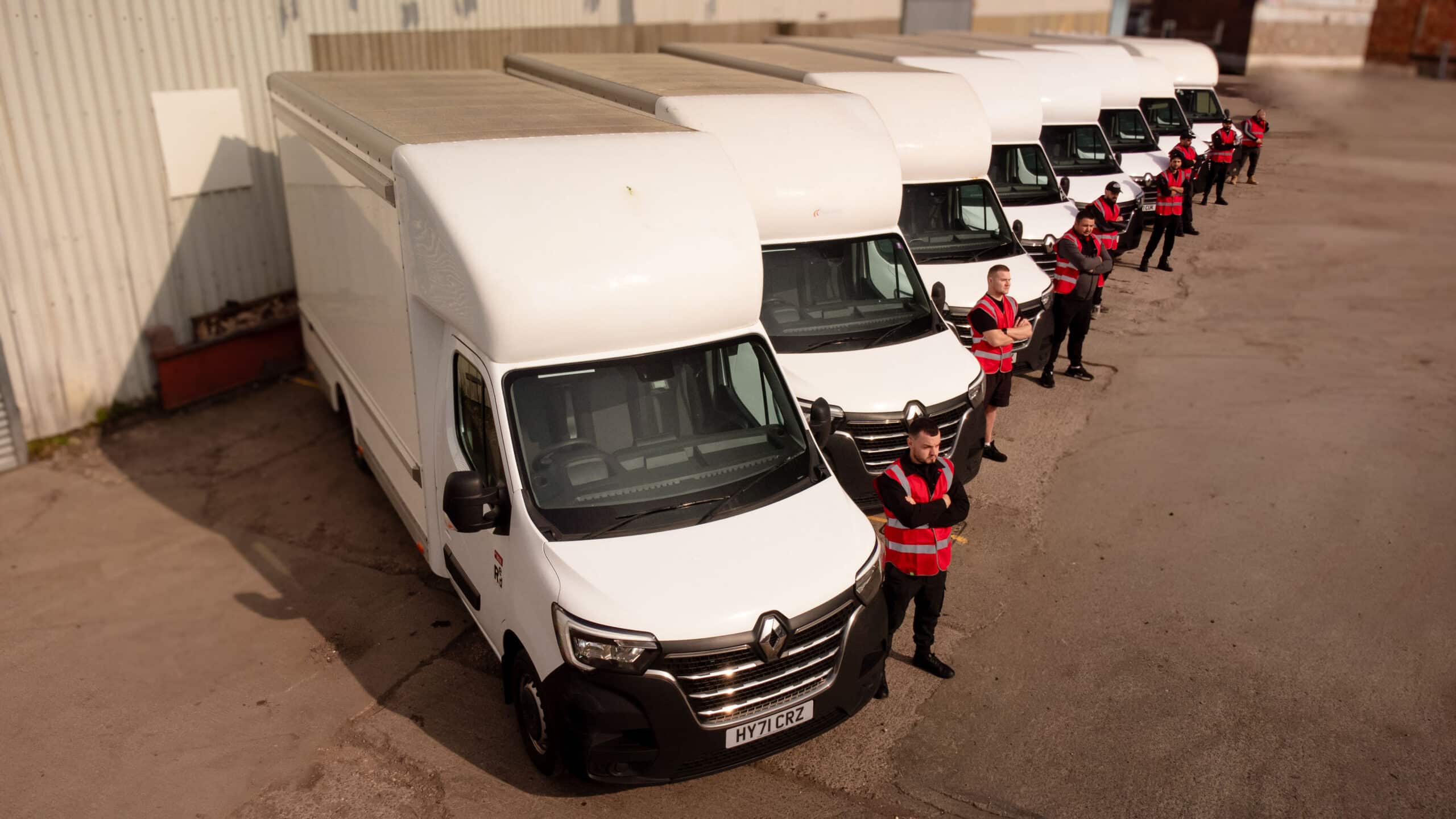 A line of white Luton vans with Proovia drivers in red hi-vis standing beside each one