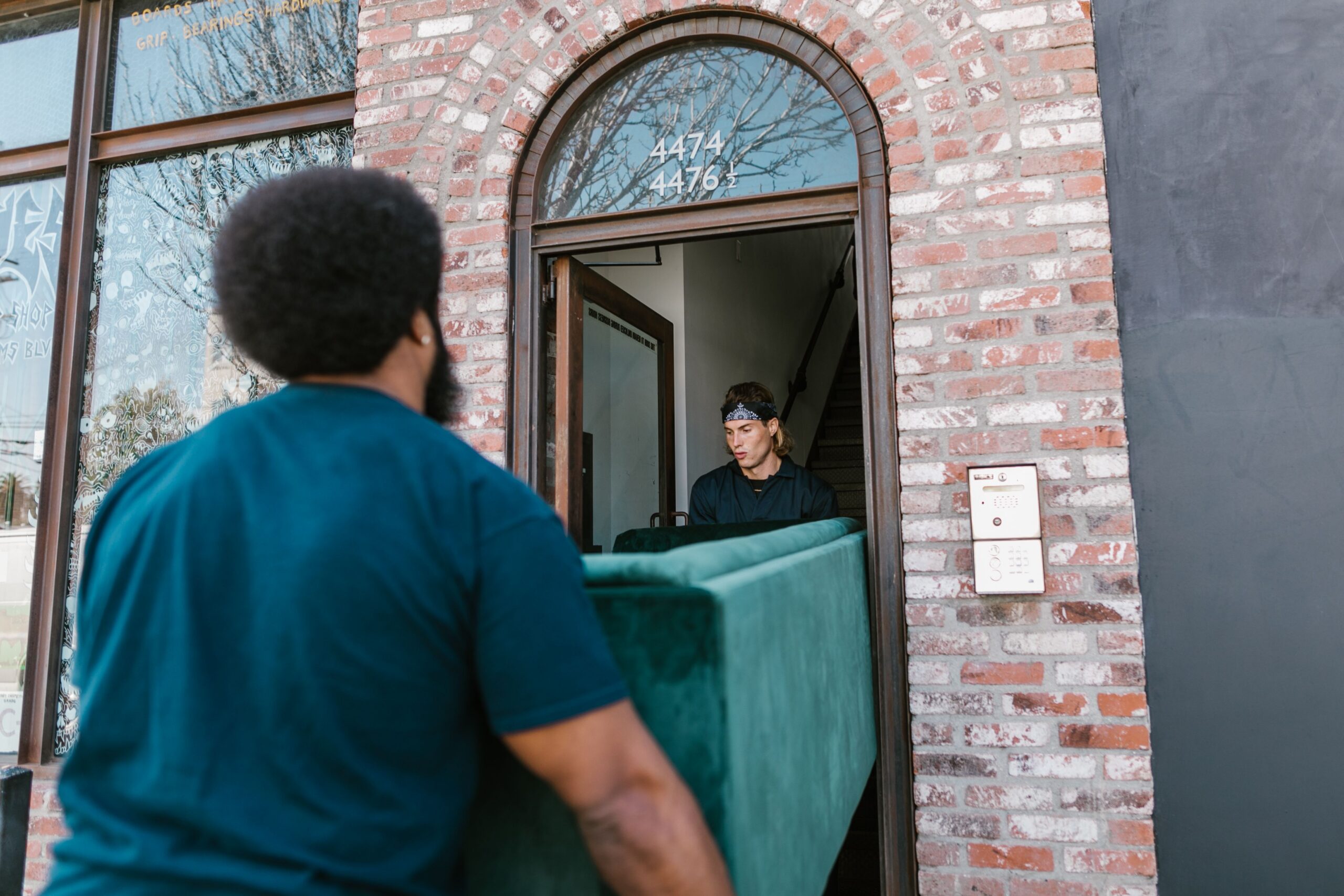 Two-person crew carrying a sofa through a doorway into a home